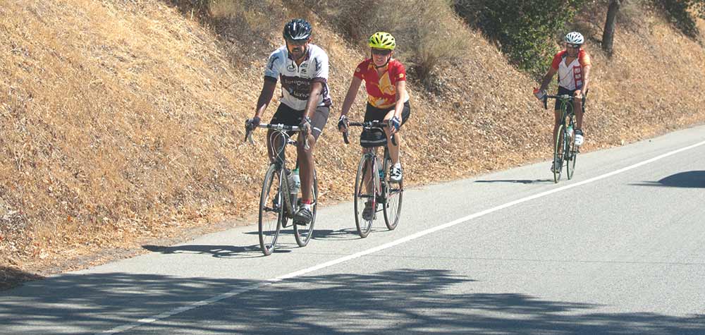 Photo of 3 bicycle riders on an empty hilly road