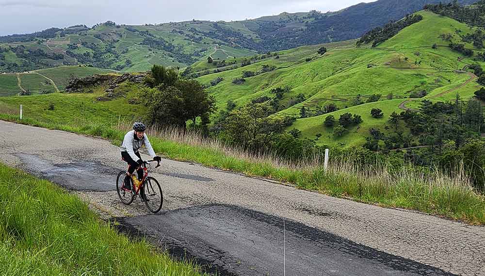 Photo of a cyclist on a narrow road surrounded by emerald green hillsœ in Sonoma County.